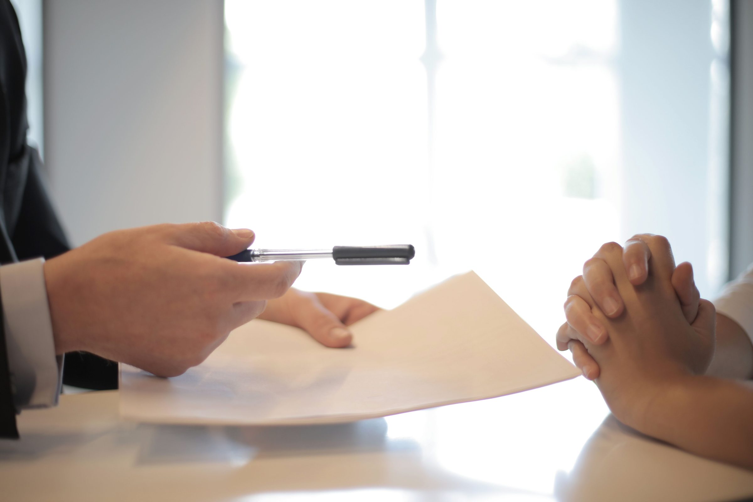 One person handing papers and a pen to another.